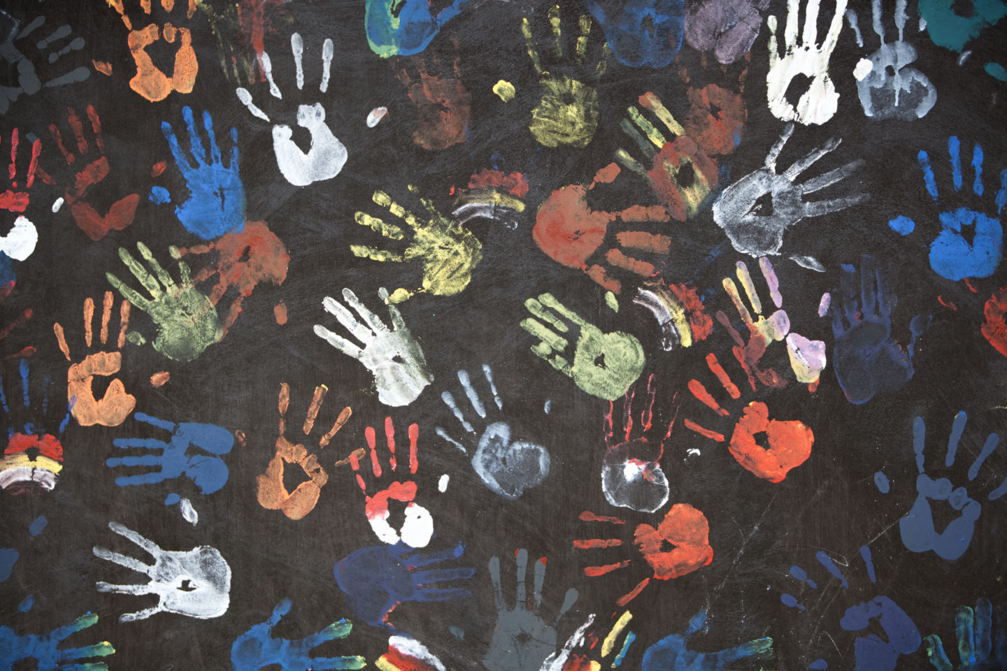 "colorful children's handprints on a textured black wall - fragment of a busstop wall in Bali, Indonesia"